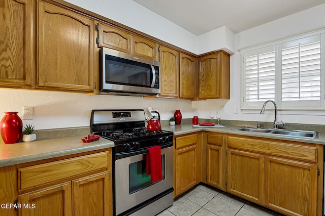 kitchen with a sink, stainless steel appliances, brown cabinetry, and light tile patterned floors