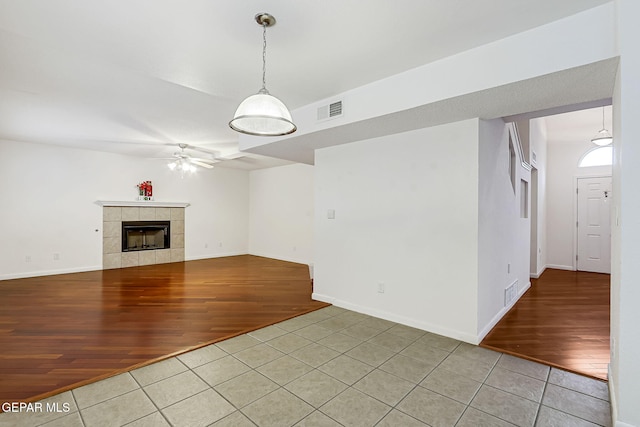 unfurnished living room featuring visible vents, baseboards, light tile patterned floors, a tile fireplace, and a ceiling fan