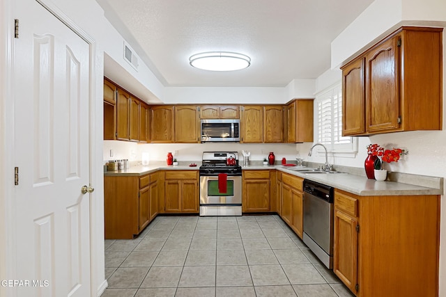 kitchen featuring brown cabinetry, visible vents, light tile patterned flooring, a sink, and appliances with stainless steel finishes