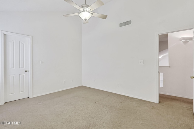 carpeted spare room featuring visible vents, baseboards, a ceiling fan, and a towering ceiling