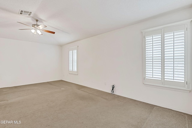 carpeted spare room with visible vents and a ceiling fan