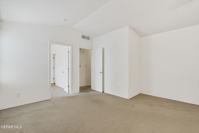 carpeted empty room with visible vents and vaulted ceiling