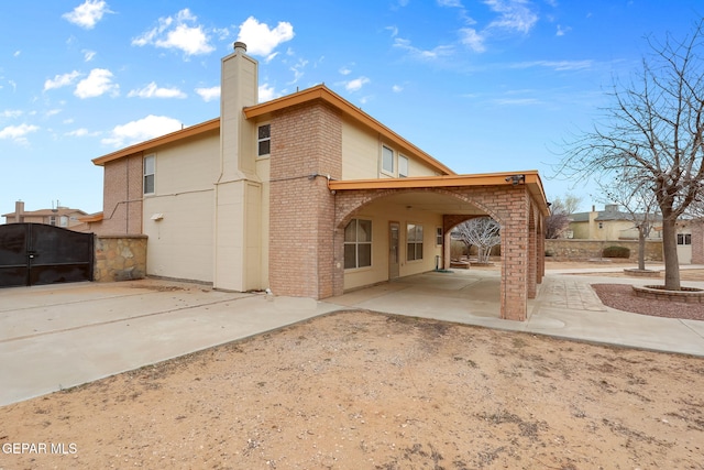 rear view of house with a gate, fence, a chimney, a patio area, and brick siding