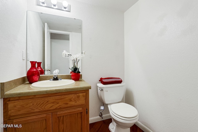 half bath with baseboards, toilet, wood finished floors, and vanity