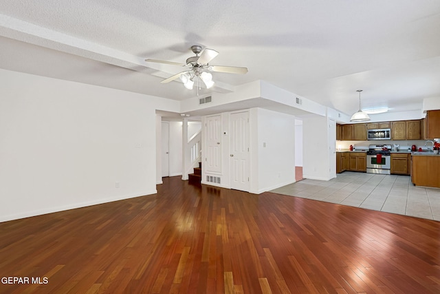 unfurnished living room with visible vents, baseboards, stairway, light wood-style floors, and a ceiling fan