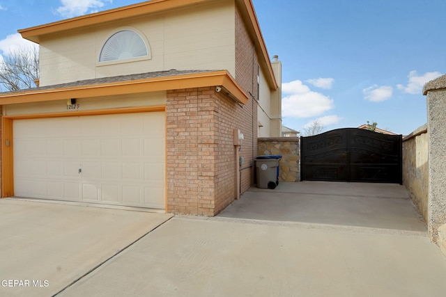 view of property exterior with a garage, brick siding, concrete driveway, and a gate