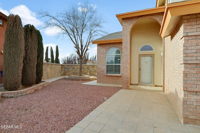 property entrance with brick siding, a patio area, a shingled roof, and fence