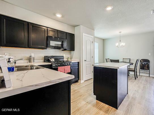 kitchen with light wood-style flooring, a kitchen island, a textured ceiling, black appliances, and pendant lighting