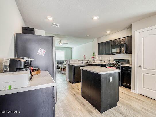 kitchen featuring black microwave, dishwashing machine, light wood-style flooring, a peninsula, and gas range