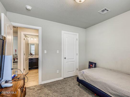 bedroom with light colored carpet, visible vents, a textured ceiling, and baseboards