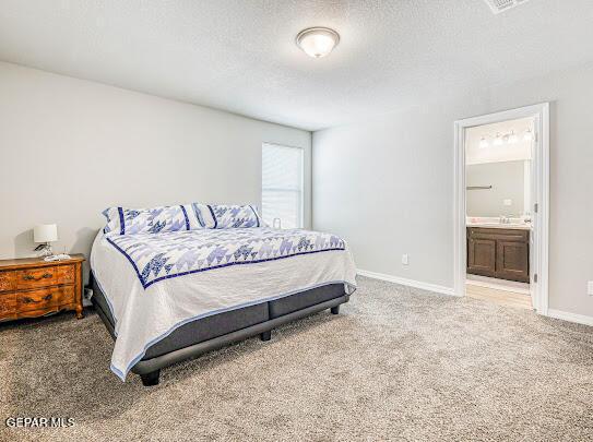 bedroom featuring carpet, ensuite bath, a textured ceiling, and baseboards