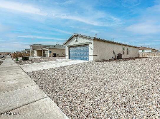 view of front of home with driveway, a garage, central AC, and stucco siding