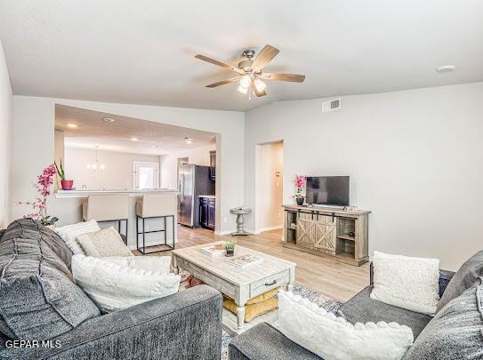 living area with visible vents, light wood finished floors, and ceiling fan with notable chandelier