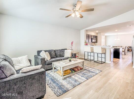 living room with vaulted ceiling, ceiling fan with notable chandelier, and light wood-type flooring