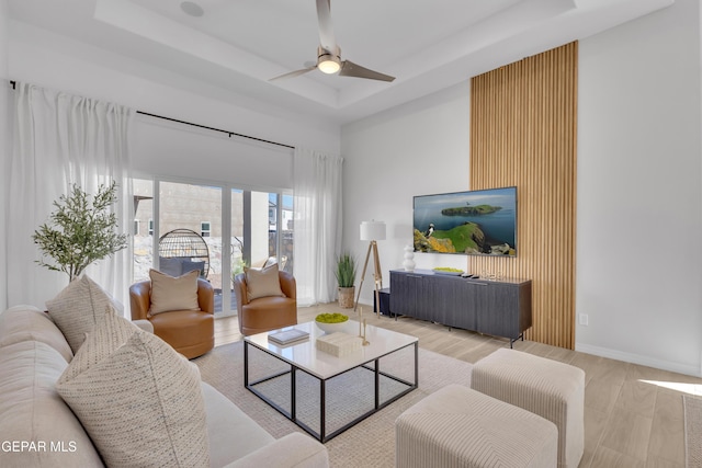 living room featuring light wood finished floors, a tray ceiling, a towering ceiling, and baseboards