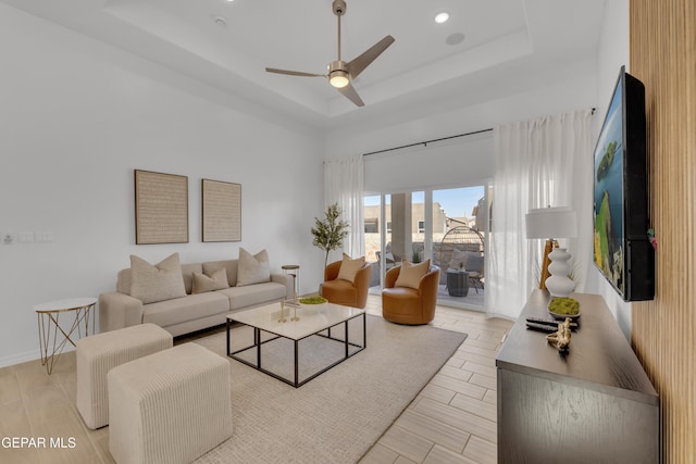 living area with a tray ceiling, a high ceiling, a ceiling fan, light wood-type flooring, and baseboards