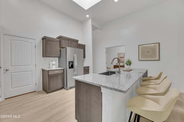 kitchen with a skylight, light wood-style floors, a kitchen bar, stainless steel refrigerator with ice dispenser, and a sink