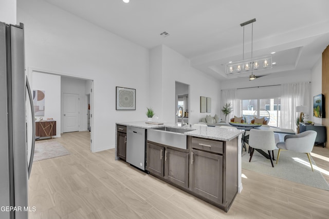 kitchen featuring open floor plan, light stone countertops, a tray ceiling, stainless steel appliances, and a sink