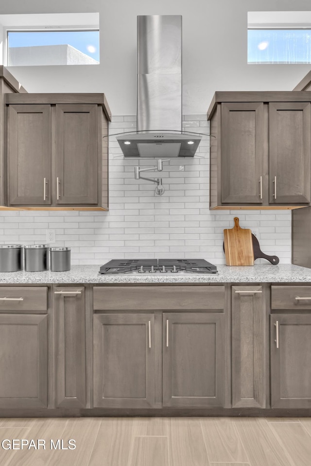 kitchen with stainless steel gas cooktop, tasteful backsplash, light stone countertops, and island range hood