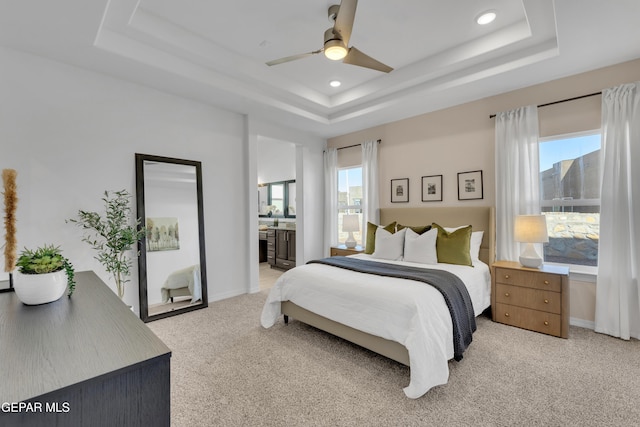 bedroom with light carpet, multiple windows, a raised ceiling, and baseboards