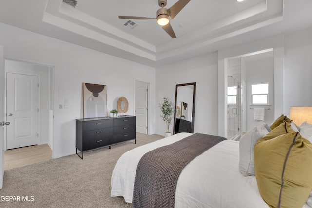 bedroom with a ceiling fan, light colored carpet, a raised ceiling, and visible vents