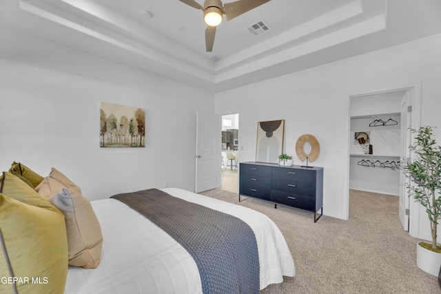 bedroom with ceiling fan, visible vents, a raised ceiling, and light colored carpet