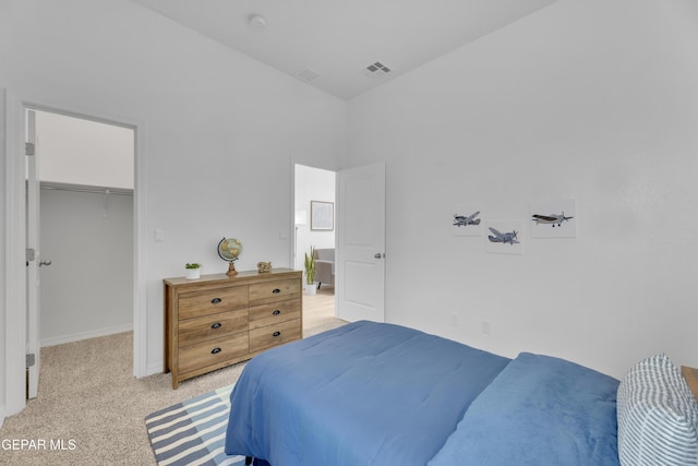 bedroom with a closet, a walk in closet, visible vents, and light colored carpet