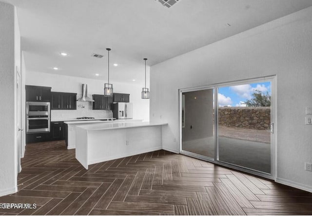 kitchen featuring baseboards, appliances with stainless steel finishes, dark cabinets, light countertops, and wall chimney range hood