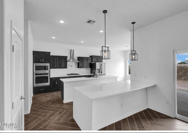 kitchen with light countertops, appliances with stainless steel finishes, wall chimney range hood, and visible vents