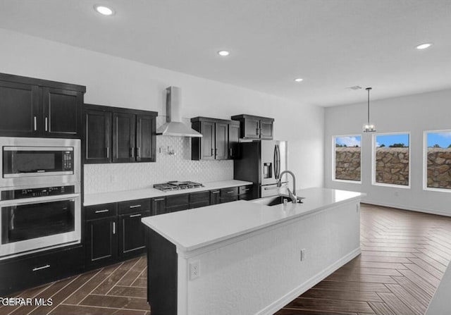 kitchen with appliances with stainless steel finishes, dark cabinetry, a sink, and wall chimney exhaust hood