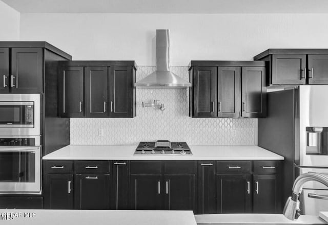 kitchen with stainless steel appliances, wall chimney range hood, dark cabinetry, and tasteful backsplash