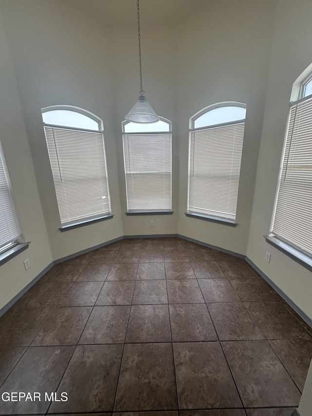 unfurnished dining area with a high ceiling, dark tile patterned floors, and baseboards