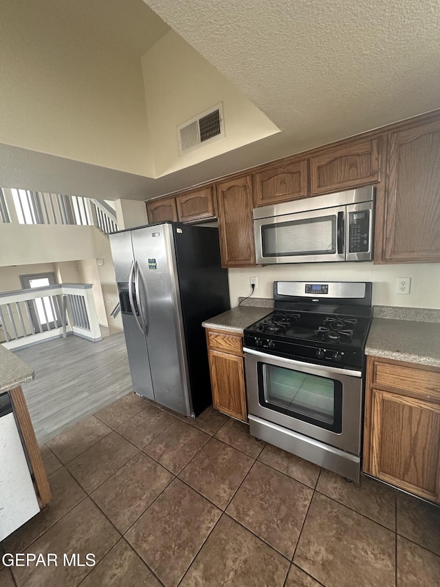 kitchen with visible vents, brown cabinetry, stainless steel appliances, a textured ceiling, and dark tile patterned floors