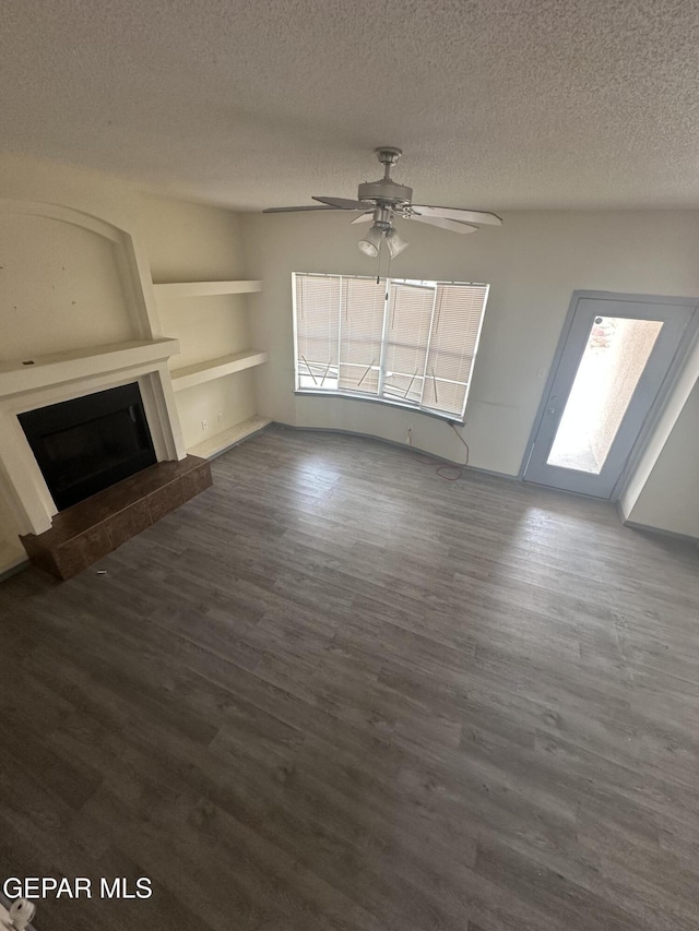 unfurnished living room with a fireplace with raised hearth, ceiling fan, dark wood-style flooring, and a textured ceiling