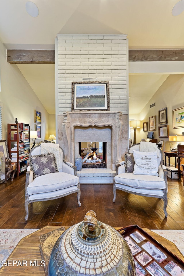 living area featuring lofted ceiling with beams, wood-type flooring, a fireplace, and visible vents