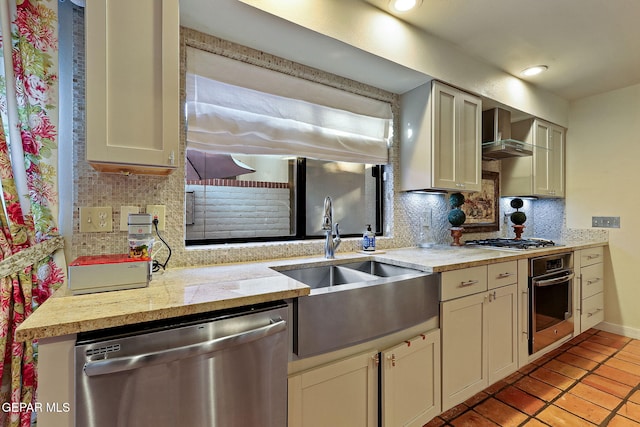 kitchen featuring light tile patterned floors, a sink, wall chimney range hood, appliances with stainless steel finishes, and backsplash