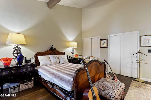 bedroom with baseboards, dark wood finished floors, a towering ceiling, multiple closets, and beam ceiling