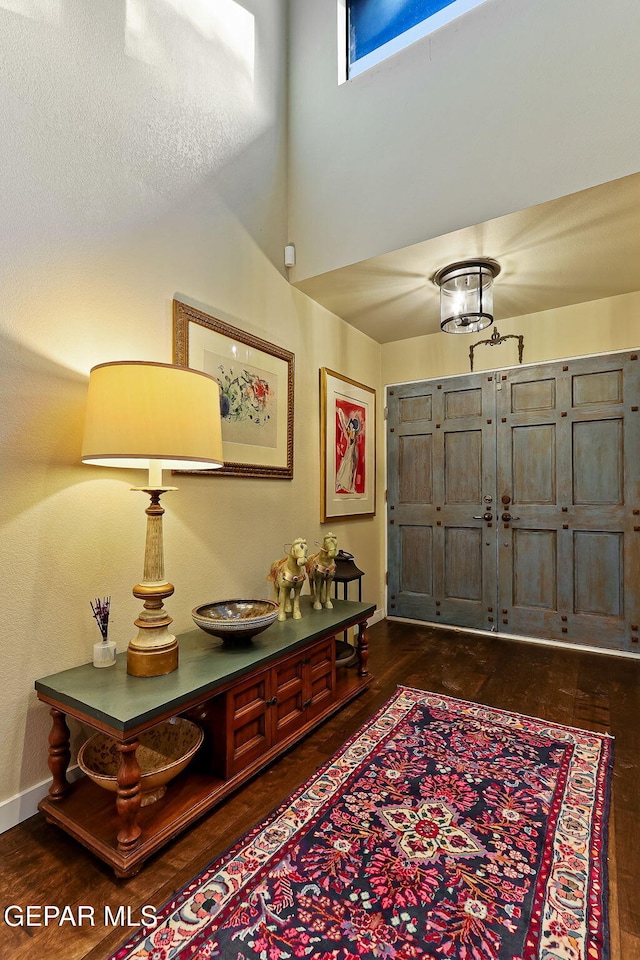 foyer entrance with a high ceiling, baseboards, and dark wood-type flooring