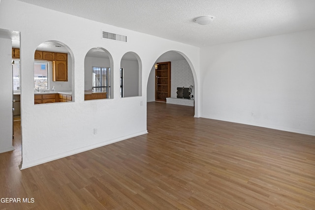 unfurnished room featuring visible vents, a textured ceiling, baseboards, and wood finished floors