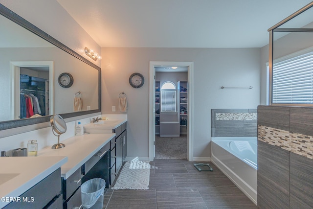 bathroom with a garden tub, double vanity, a sink, and a walk in closet