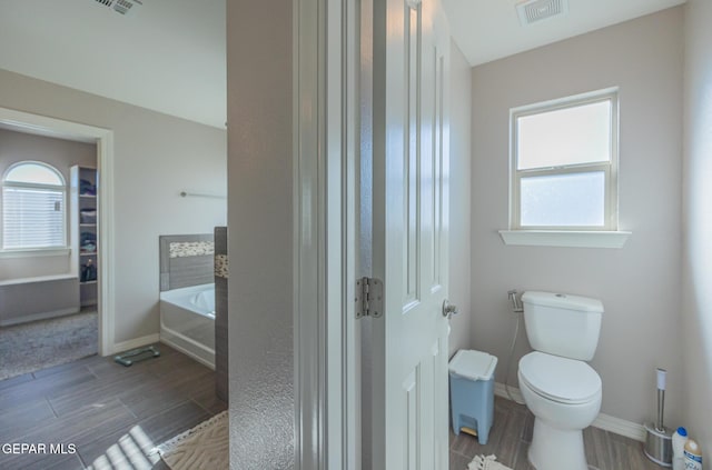 full bathroom featuring wood tiled floor, a garden tub, visible vents, and toilet