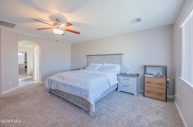 carpeted bedroom with arched walkways, ceiling fan, visible vents, and baseboards