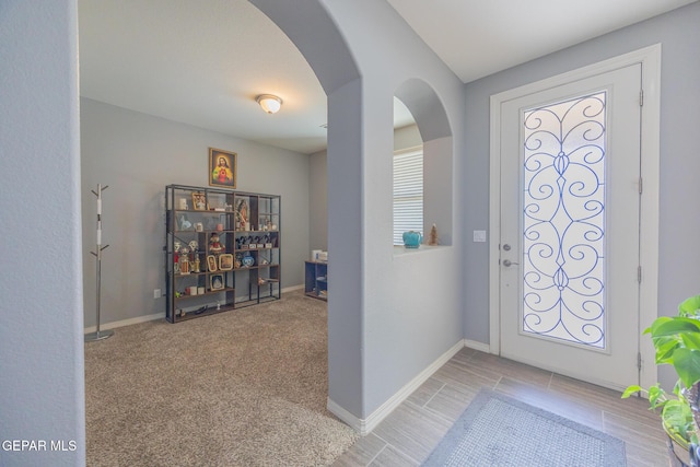 foyer entrance featuring arched walkways, light colored carpet, and baseboards