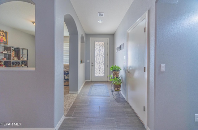 doorway to outside featuring arched walkways, visible vents, and baseboards