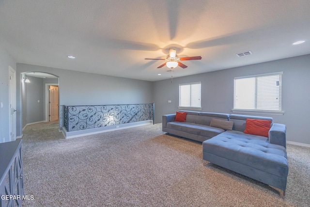 carpeted living area featuring visible vents, arched walkways, baseboards, ceiling fan, and a textured ceiling