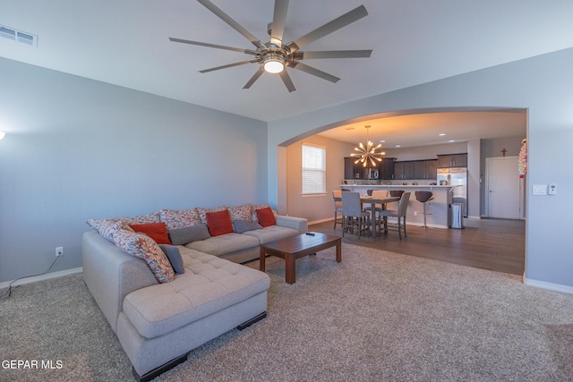 living area with arched walkways, ceiling fan with notable chandelier, visible vents, baseboards, and carpet