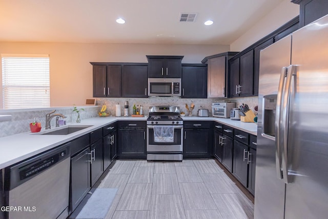 kitchen featuring visible vents, appliances with stainless steel finishes, a sink, light countertops, and backsplash