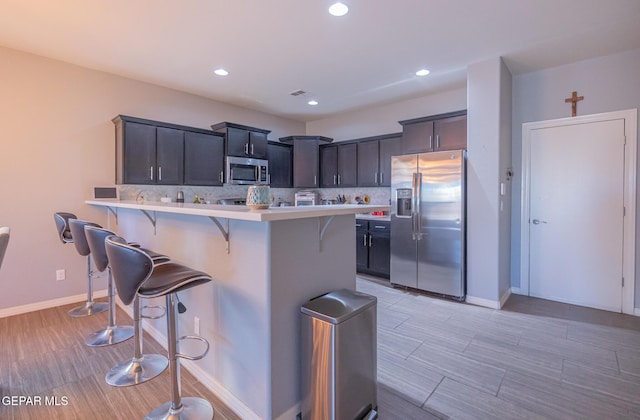 kitchen featuring stainless steel appliances, a breakfast bar area, light countertops, and backsplash