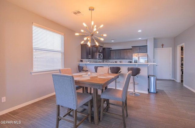 dining area featuring a chandelier, visible vents, baseboards, and wood finished floors