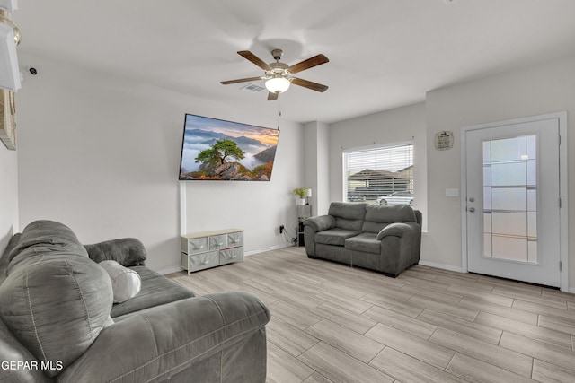 living room with light wood-style flooring, visible vents, baseboards, and a ceiling fan